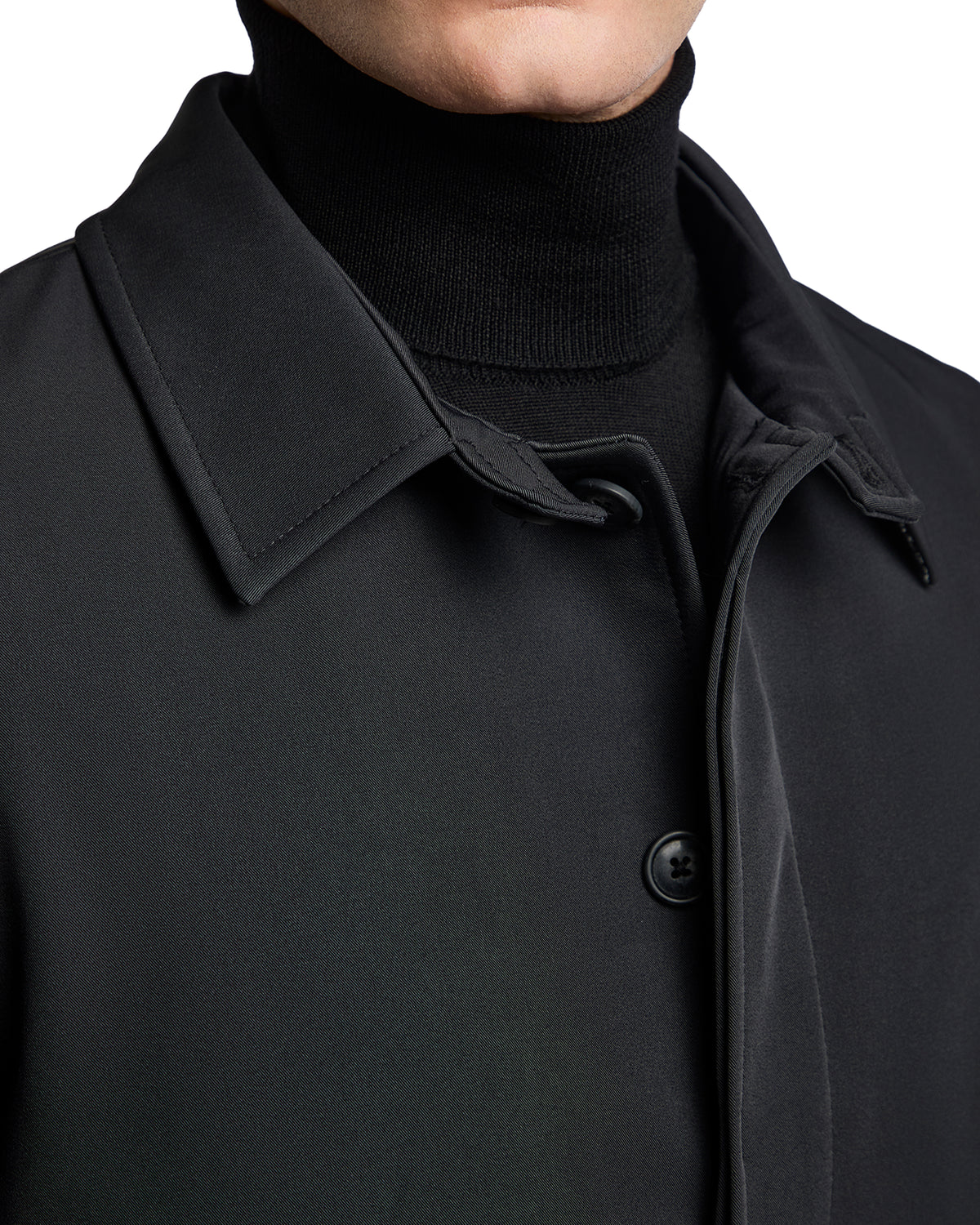Black tailored coat with a sleek silhouette, featuring a classic collar and button closure, paired with a black turtleneck.